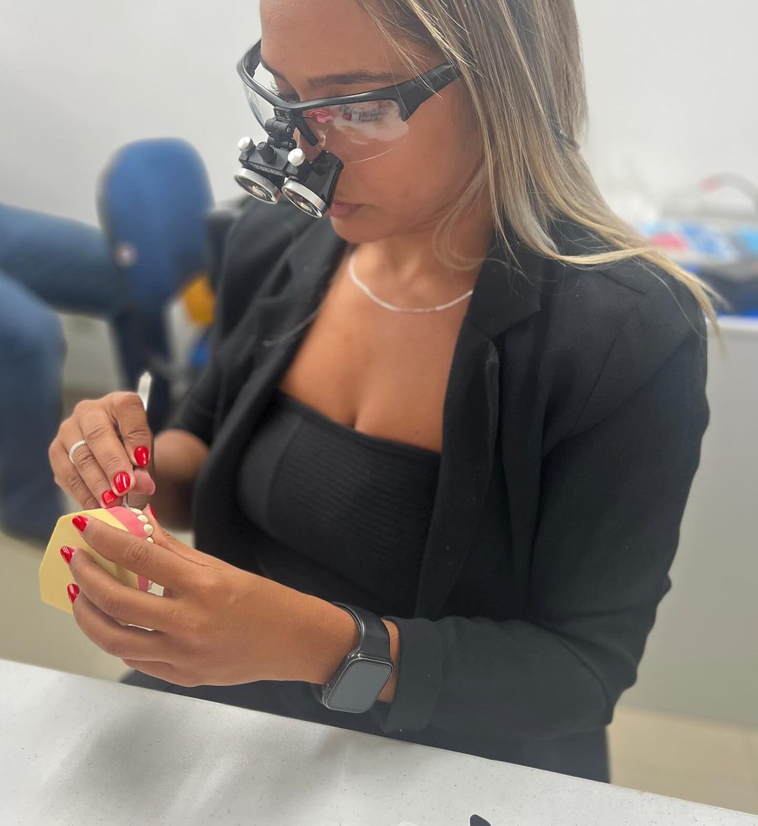 Dra. Dyene Oliveira usando lupa de aumento enquanto trabalha em um modelo dental.